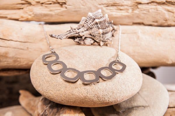 Collana con anelli geometrici in acciaio su un sasso di spiaggia