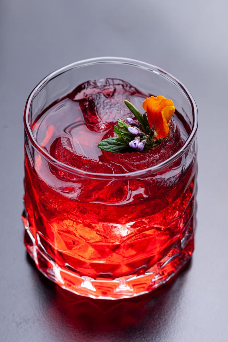 Cocktail rosso con fiori ed erbe aromatiche su fondo grigio