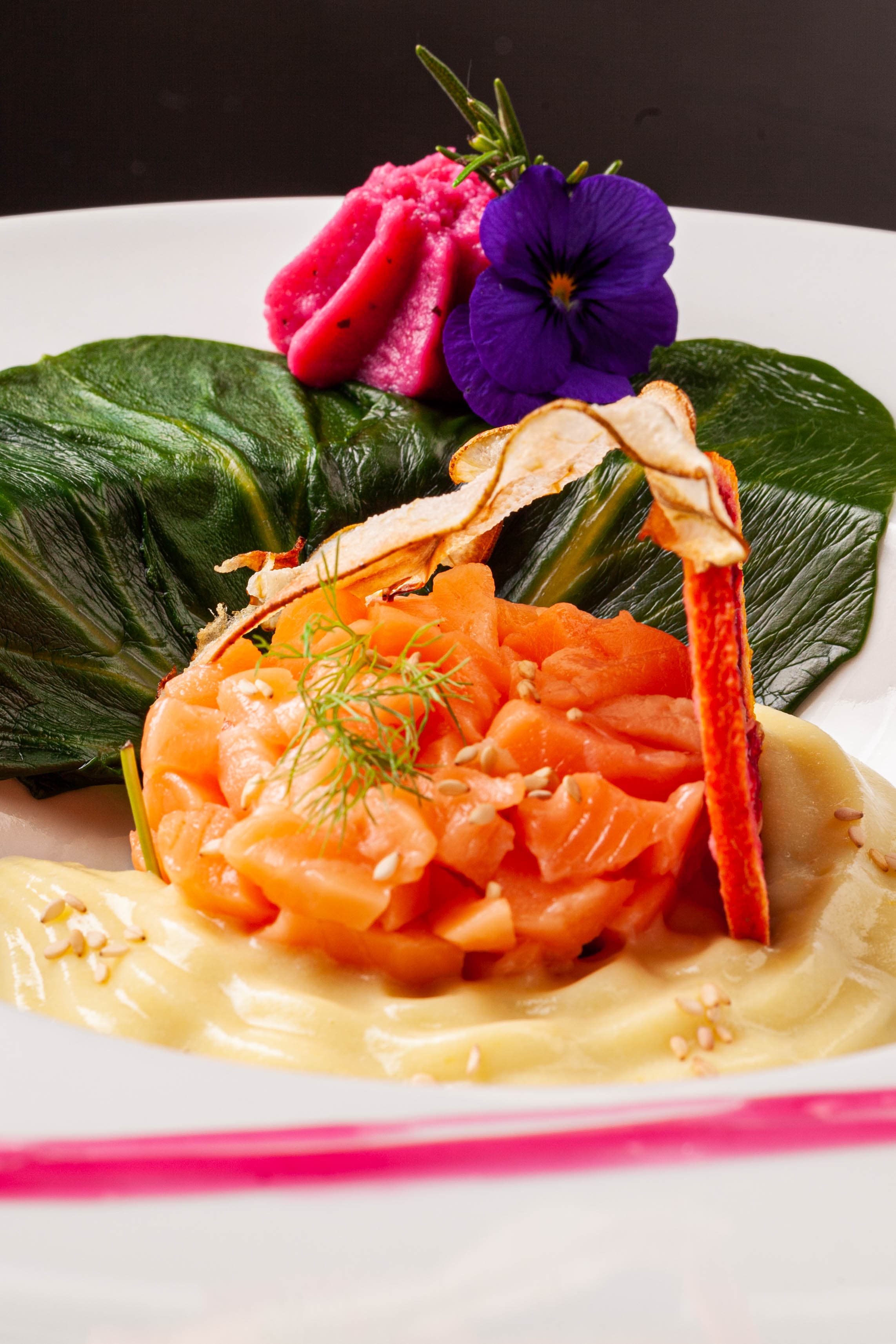 Salmone tagliato fresco su foglia di ibisco, mousse, fiori viola e rosa — la grazia della semplicità